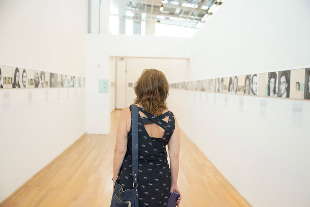Mujer observando exposición de retratos en galería de arte.